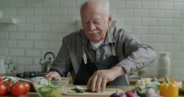 Neşeli büyükbabanın evde öğle yemeği hazırlarken sebze salatası pişirmesi. Vejetaryen yaşam tarzı ve yemek hazırlama konsepti.