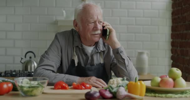 Ηλικιωμένος Άντρας Μιλάει Στο Κινητό Τηλέφωνο Και Μαγειρεύει Σαλάτα Για — Αρχείο Βίντεο