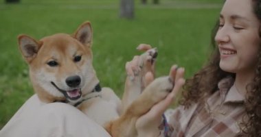 Neşe dolu genç bir kadının Shiba Inu köpeğiyle oynaması ve parkta eğlenmesi. Hayvan ve insan birlikte yaz gününün tadını çıkarıyor..