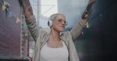 Şehirde dans eden ve kulaklıkla müzik dinleyen güzel bir kadının yavaş çekim portresi. Gençlik kültürü ve eğlence etkinliği konsepti.