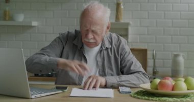 Evdeki masada oturan kıdemli adam ödemeye yoğunlaşmış paraları sayarak faturaları kontrol ediyor. Emeklilik finansmanı ve ev konsepti.