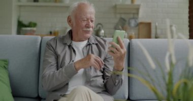 Üst düzey bir adam evdeki oturma odasında akıllı telefon kullanarak çevrimiçi video görüşmesi yapıyor. İletişim ve modern teknoloji kavramı.