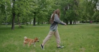 Parkta Shiba Inu köpeğiyle koşan genç bir kadının hareketsiz yaşam tarzının keyfini çıkarması. Eğlence etkinliği ve hayvan sahibi konsepti.