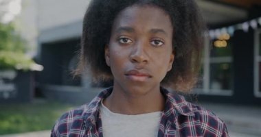 Şehirde dikilip kameraya bakan üzgün Afrikalı Amerikalı kadının yavaş çekim portresi. İnsani duygu ve milenyum konsepti.