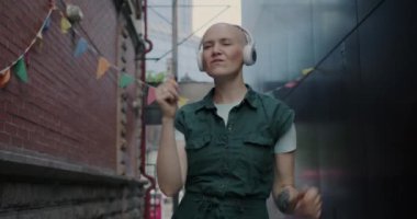 Şehirde dans eden, kulaklıkla müzik dinleyen neşeli bir kadının yavaş çekim portresi. Mutluluk ve yaşam tarzı kavramı.