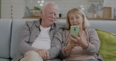 Neşeli yaşlı çift ve kadın akıllı telefon ekranı araklıyor ve evdeki kanepede rahatça konuşuyorlar. Aygıt ve aile yaşam tarzı kavramı.