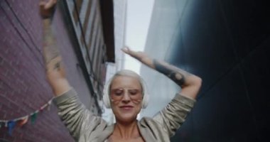 Kulaklık takan, sokakta dans eden ve boş zamanlarında müzik dinleyen güzel bir kızın yavaş çekimde portresi. Gençlik ve boş zaman eğlence konsepti.