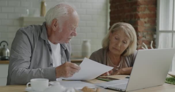 Idősebb Házaspár Ellenőrzi Fizetési Számlákat Okostelefon Számlázási Költségekkel Otthon Konyhában — Stock videók