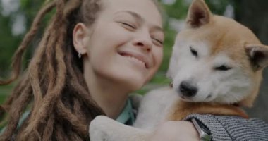 Sevgi dolu bir kadının sevimli Shiba Inu köpeğini öptüğü ve yaz günü dışarıda sevgisini ve mutluluğunu ifade ettiği yakın plan portresi. Hayvan ve sevecen insan konsepti.