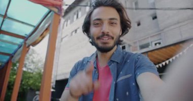 Neşeli Orta Doğulu bir adam çevrimiçi video görüşmesi yapıyor. Yaz şehrinde dışarıda konuşuyor ve el kol hareketi yapıyor. İletişim ve modern yaşam tarzı kavramı.