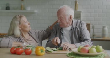 Emekli çift salata hazırlıyor sebze yiyor ve evde, mutfakta konuşuyor. Aile sohbeti ve sağlıklı beslenme kavramı.