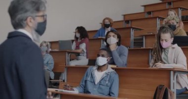 Yüzü maskeli bir üniversite öğretmeni covid-19 küresel salgını sırasında bir grup öğrenciye ders veriyor. Sağlık ve Eğitim Konsepti.