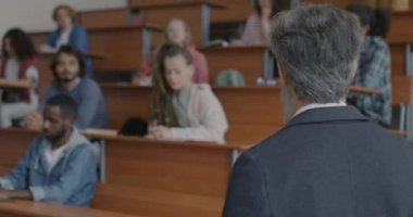 Üniversite öğretmeni sınıftaki öğrencilere bakarak yeni bilgileri açıklıyor ve işaret ediyor. İletişim ve eğitim kavramı.