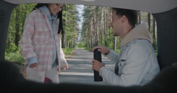車で休暇を楽しんで座って魔法瓶からお茶を飲む若いカップルの観光客のスローモーション 自動車旅行と旅行のコンセプト — ストック動画