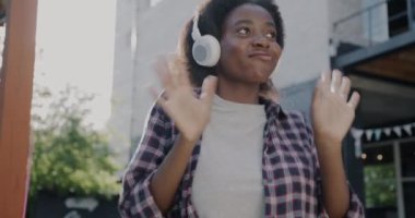 Afrika kökenli neşeli Amerikalı kadının yavaş çekimde çekilmiş bir portresi. Kulaklık takmış, dans ediyor ve şehirde eğleniyor. İnsanlar ve eğlence konsepti.