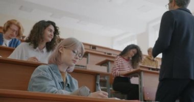 Üniversite profesörü genç insanlar dinlerken ve yazarken bir grup erkek ve kadına ders veriyor. Eğitim ve sınıf kavramı.