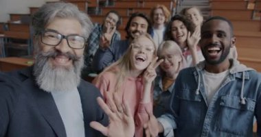 Üniversite sınıfında eğlenen neşeli öğretmenle selfie çeken mutlu öğrencilerin yavaş çekimleri. Eğitim ve eğlence aktivite konsepti.