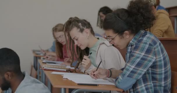 教師が歩いている間 教室の机に座ってテスト勉強を書いている若者のグループ 大学教育と知識評価の概念 — ストック動画