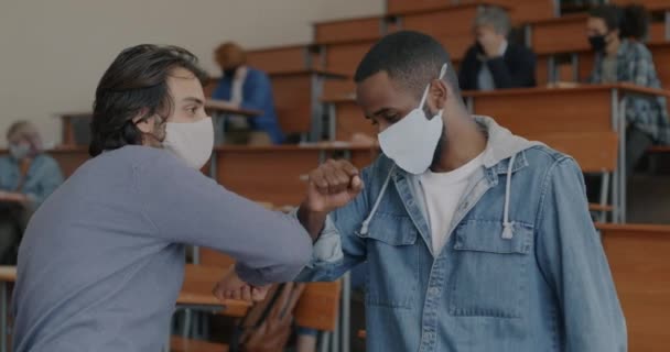 Młodzi Mężczyźni Maskach Witają Się Łokciami Rozmawiają Klasie Uniwersyteckiej Podczas — Wideo stockowe