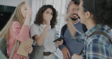 Neşeli arkadaşlar üniversitede tanışan erkekler ve kadınlar beşlik çakıyor. Akıllı telefon kullanarak konuşuyor ve gülüyorlar. Arkadaşlık ve eğitim kavramı.