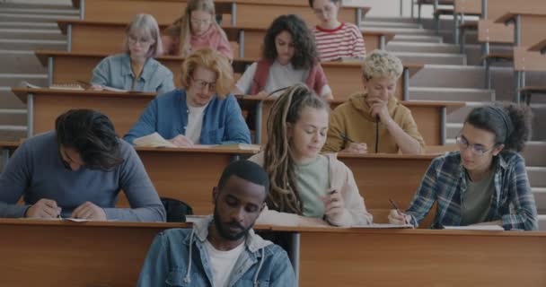 大学の教室での試験に焦点を当てた試験を書く男性と女性の学生の多文化グループ 教育と若者の概念 — ストック動画