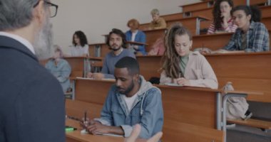 Erkek ve kadın öğrenciler çeşitli gruplar halinde üniversitede okuyan profesörü dinliyorlar. Yüksek öğrenim ve gençlik kavramı.
