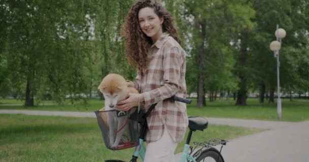 自転車の横に立つ若い女性のスローモーションポートレートと自転車バスケットに柴犬を保持します アクティブなライフスタイルと動物のコンセプト — ストック動画