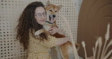 Yavaş çekimde, evcil hayvan dostu kafede kameraya bakıp Shiba Inu köpeğini kucaklayan genç bir kadının portresi. Hayvanlar ve insanlar kavramı.