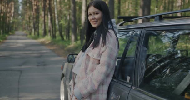 站在现代汽车旁边的快乐的年轻女士的画像 背景是秋天的森林 旅行和运输概念 — 图库视频影像
