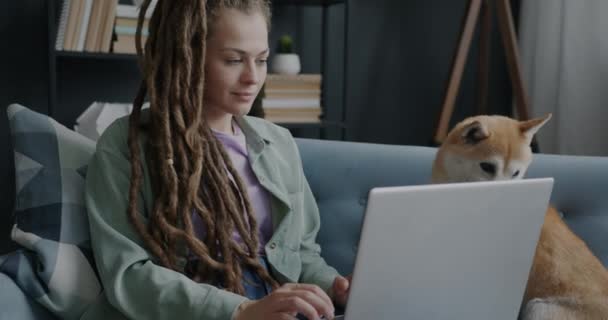 年轻的女士用笔记本电脑坐在沙发上 带着漂亮的狗在家里工作 家畜和现代生活方式概念 — 图库视频影像