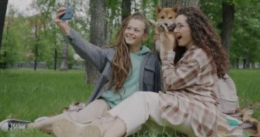 Mutlu kız kardeşler Shiba Inu 'nun köpeğiyle selfie çekip parkta akıllı telefon kamerasıyla eğleniyorlar. Fotoğraf ve hayvanlar konsepti.