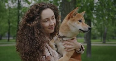 Shiba inu köpeği tutan genç bir kadının portresi evcil hayvanla konuşuyor sonra da kameraya bakıyor ve yaz parkında gülümsüyor. Hayvanlar ve doğa kavramı.