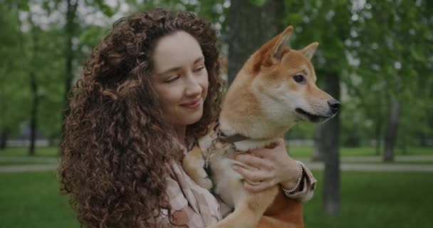 柴犬を飼っている若い女性がペットと話をし カメラを見て夏の公園で笑っている姿が描かれています 動物と自然概念 — ストック動画