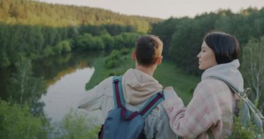Bir çift turistin dağdan orman nehri izlemesi ve yaz akşamları konuşması. Doğa ve turizm kavramı.