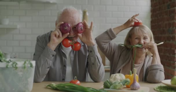 一对老夫妇在家里拿着蔬菜在厨房里玩乐 脸上挂着滑稽的笑脸 动作缓慢 食品杂货店和老年人概念 — 图库视频影像