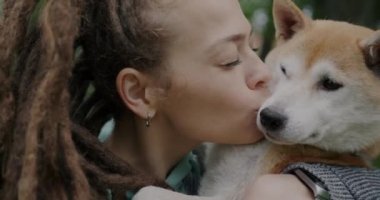 Neşeli kızın Shiba Inu köpeğini öptüğü ve doğal arka planda hayvana sevgisini ifade ettiği yakın plan. Sevecen insanlar ve doğa konsepti.