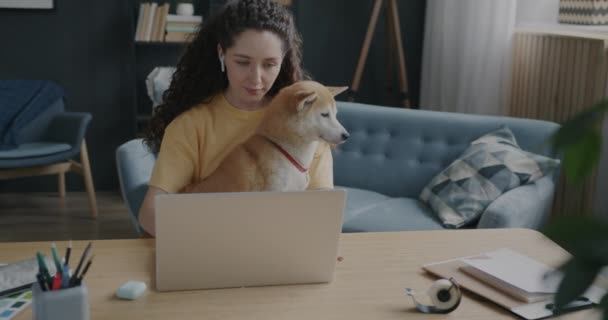 女学生在家里用笔记本电脑慢吞吞地走着 在公寓的桌子上抱着可爱的小狗狗 网上教育和家畜概念 — 图库视频影像