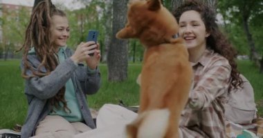 Genç bir kadının akıllı telefondan arkadaşlarıyla parkta eğlenirken çektiği videoyu yavaş çekimde izlemesi. Evcil hayvanlar ve eğlence konsepti.