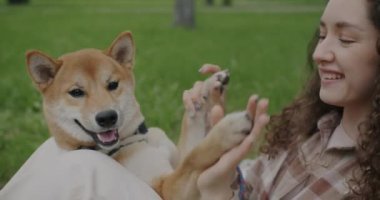 Neşe dolu genç bir kadının Shiba Inu köpeğiyle oynaması ve parkta eğlenmesi. Hayvan ve insan birlikte yaz gününün tadını çıkarıyor..