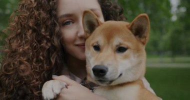 Güzel bir kadının yakından çekilmiş portresi. Elinde tapılası Shiba Inu köpeği var. Yaz günü parkta kameraya bakıyor. Hayvan ve insan kavramı.