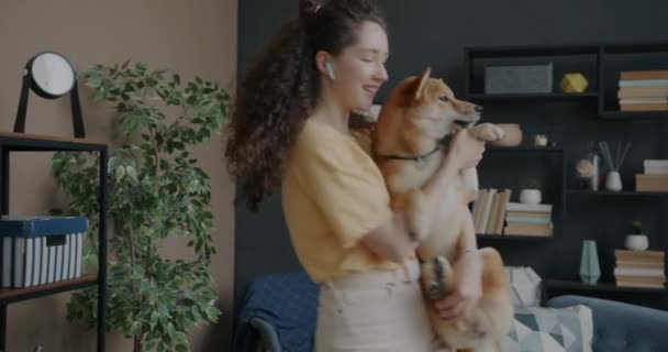 イヤホンで音楽を聴き 自宅で柴犬と踊る若い女性のスローモーション 家畜と娯楽の概念 — ストック動画
