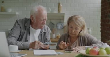 Mutsuz yaşlılar, pahalı faturaları öderken mutfaktaki ödeme belgelerini kontrol ederken para sayıyorlar. Aile bütçesi ve yoksulluk kavramı.