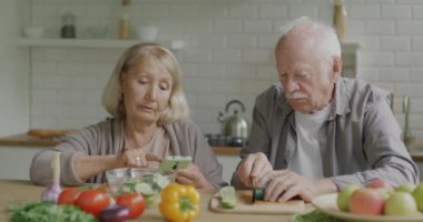 Erkek ve kadın kıdemli çift evde salata pişiriyor ve tarifi akıllı telefondan kontrol ediyor. Beslenme ve modern teknoloji konsepti.