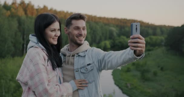 在山林里 一对男女快乐的夫妇拿着智能手机相机自拍 在户外接吻 照片和旅游概念 — 图库视频影像