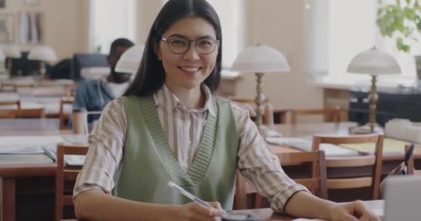 Портрет Радостной Азиатской Студентки Очках Повседневной Одежде Сидящей Университетской Библиотеке — стоковое видео
