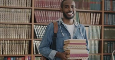 Kolej kütüphanesinde elinde eğitimle tatmin edici kitaplar tutan mutlu Afrikalı Amerikalının yavaş çekimde portresi. Gençlik ve okuma edebiyat kavramı.