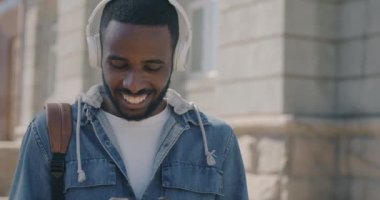 Kulaklık takan, akıllı telefon kullanan ve müzik dinleyen Afrikalı Amerikalı adamın yavaş çekim portresi. Gençlik ve modern yaşam tarzı kavramı.