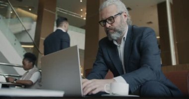 Olgun iş adamı, otel lobisindeki aktivitelere odaklanmış dizüstü bilgisayarla çalışıyor. İnsanlar ve modern teknoloji kavramı.