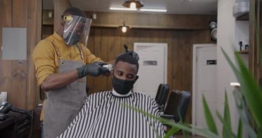 Üniformalı berber, tıbbi maske ve eldivenli berber dükkanında tıraş olan erkek müşteri. Corona virüsü salgını ve sağlık hizmeti kavramı.