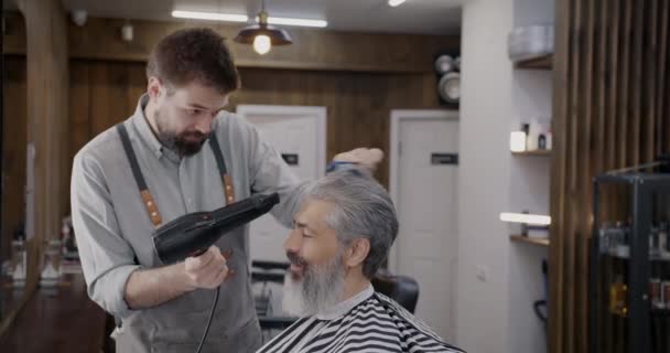 在现代理发店 专业理发师刷头发 使用烘干机护理成熟的顾客 男性沙龙概念中的美容程序 — 图库视频影像